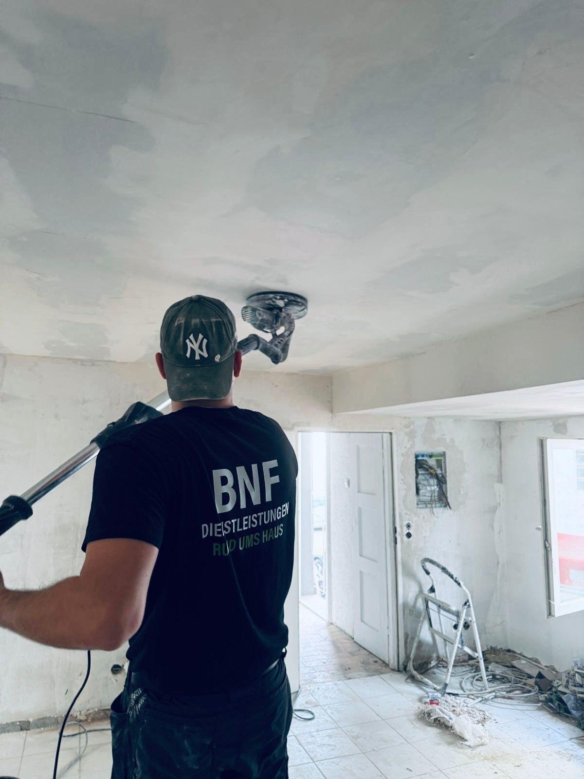Arbeiter in schwarzem BNF Shirt und Yankees Cap bei Presslufthammer-Arbeiten an weißer Decke