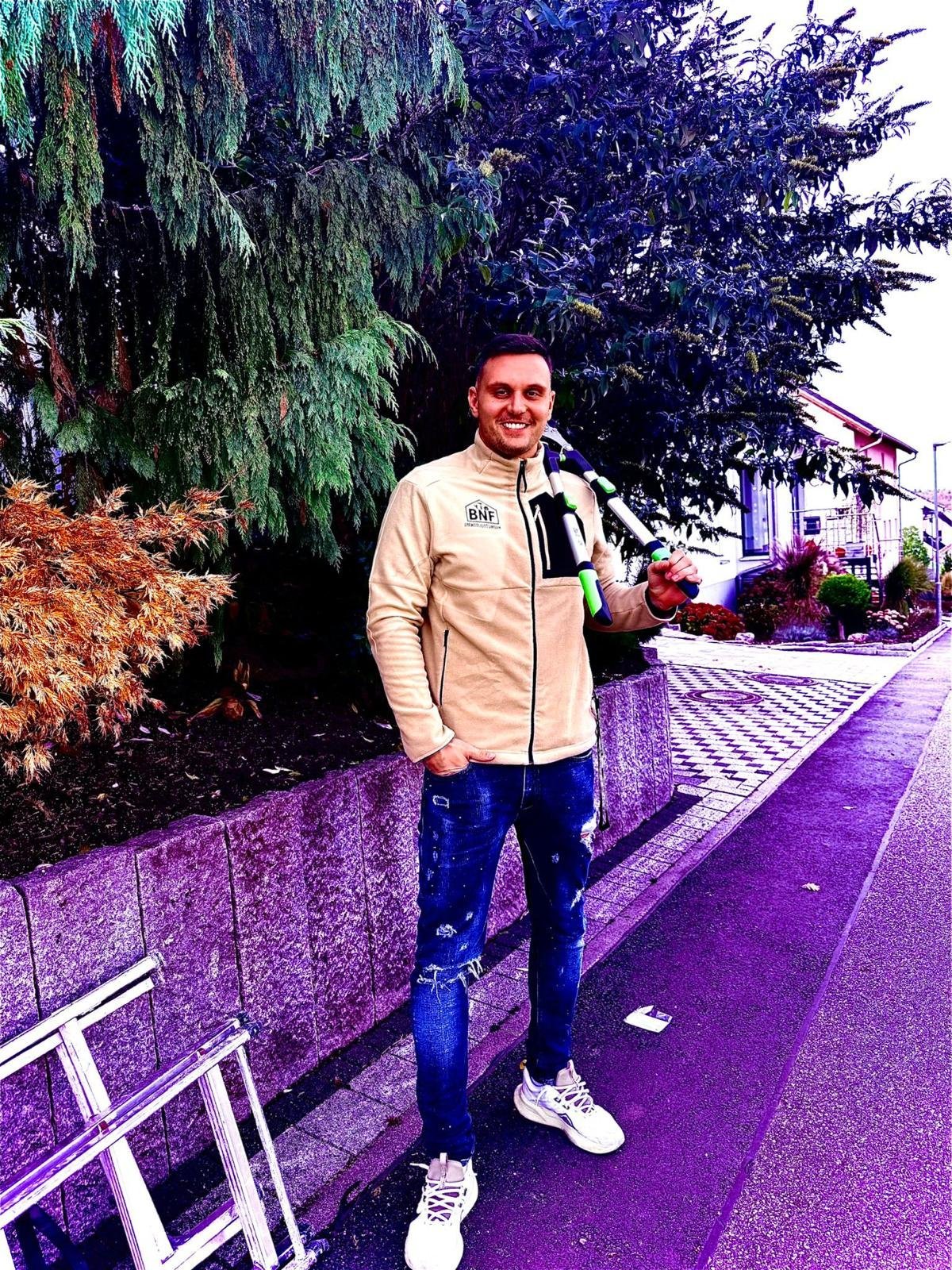 Mann auf lila Pfad mit Ziersträuchern und Gebäuden im Hintergrund