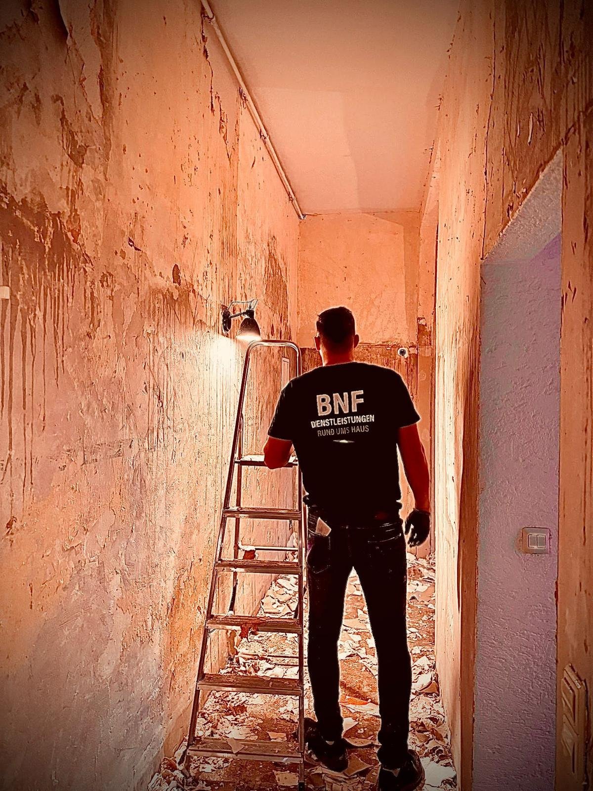 Arbeiter auf Leiter in enger heruntergekommener Halle mit abblätternden orange-rosa Wänden während Renovierung